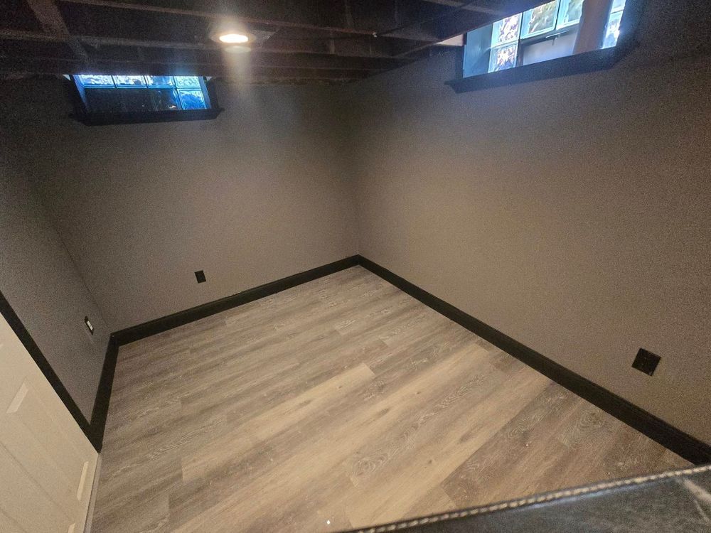 A finished basement with smooth painted walls, trim, and new flooring